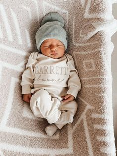 a baby is laying on a blanket wearing a blue hat and white shirt that says garrett lane