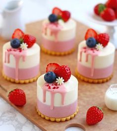 mini cheesecakes decorated with strawberries and blueberries on a cutting board next to milk