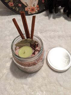 a jar filled with cinnamon sticks next to a metal container on a white tablecloth