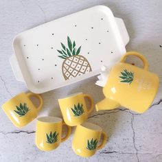 a yellow tea set with pineapple design on the front and four mugs next to it