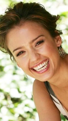 a woman smiling and posing for the camera with green leaves in the back ground behind her