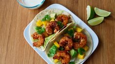 two tacos with shrimp and mango on a plate next to a glass of milk