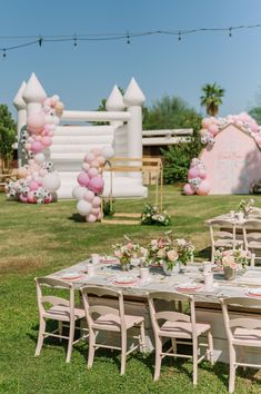 a table set up for a party with balloons and flowers on the lawn in front of it