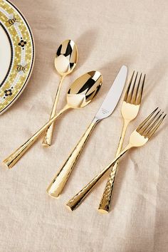 three forks, two spoons and one knife on a table with a plate in the background