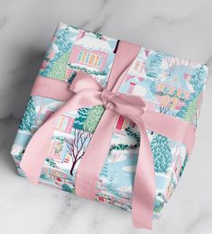 a gift wrapped in pink ribbon on top of a marble surface with trees and houses