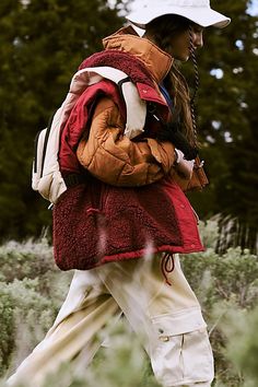 a woman walking in the grass with a backpack on her back and she's wearing a white hat