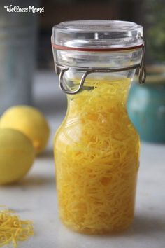 a glass jar filled with yellow noodles on top of a white counter next to lemons