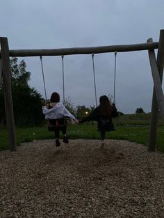 two children sitting on swings in a park at dusk, one holding the other's arm