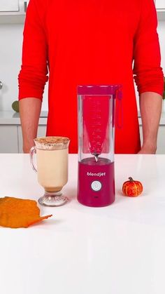 a man standing in front of a blender on top of a counter next to a cup of coffee