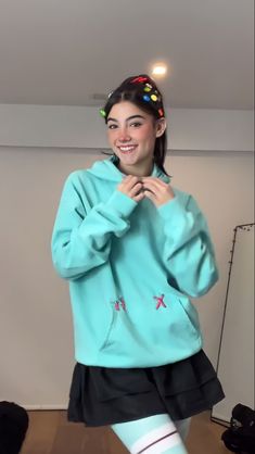 a woman in a blue sweatshirt and black skirt posing for the camera with her hands on her hips