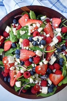 a salad with spinach, strawberries, blueberries and feta cheese in a wooden bowl