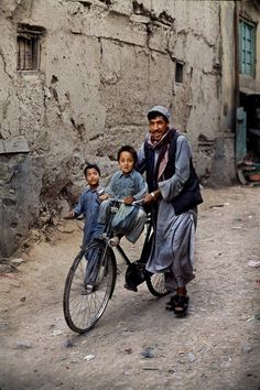 a man riding a bike with two children on it in front of an old building