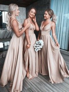 three beautiful women standing next to each other in long dresses and one is holding a bouquet