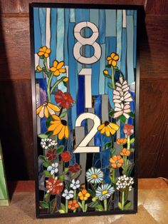 a stained glass clock with flowers and numbers on it's side, in front of a wooden wall