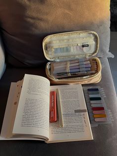 an open book sitting on top of a couch next to some markers and pencils