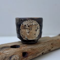 a black and white cup sitting on top of a piece of wood