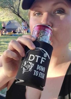 a woman is drinking from a can in the park while wearing a baseball cap and black tank top