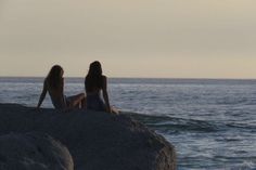 two women sitting on rocks looking out at the ocean