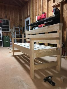 a wooden bed frame in a garage with tools on the floor and other items around it