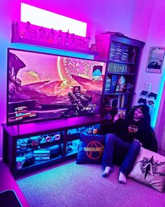 a person sitting on the floor in front of a large screen tv with purple lighting