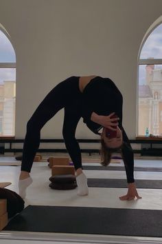 a woman in black shirt doing a handstand on yoga mat with windows behind her