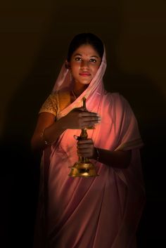 a woman in pink sari holding a golden object with her hand and smiling at the camera