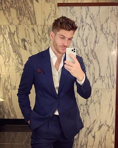 a man in a suit taking a selfie with his cell phone while standing next to a marble wall