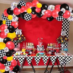 a table topped with lots of balloons next to a red and black wall covered in checkered paper