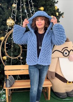 a woman standing in front of a christmas tree wearing a blue cardigan sweater and jeans