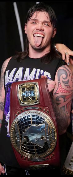 a man in a black shirt holding up a red and gold wrestling belt with his mouth open