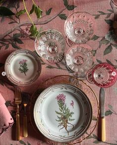 the table is set with plates, silverware and pink napkins on top of it