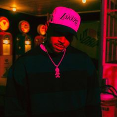 a man wearing a pink hat standing in front of a neon sign with the word lakers on it