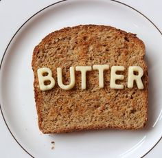 a piece of bread with the word butter spelled on it sitting on a white plate