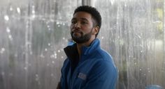 a man standing in front of a window with rain coming down on him and his head tilted to the side