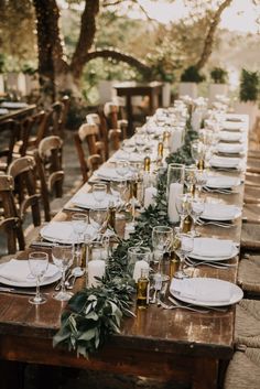 a long table with white plates and silverware is set up for an outdoor dinner