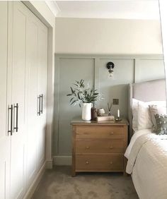 a bed room with a neatly made bed and a plant on top of the dresser