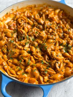 a blue skillet filled with pasta and meat covered in sauce, garnished with parsley