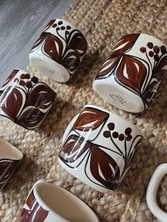 four coffee cups sitting on top of a rug next to two mugs with handles