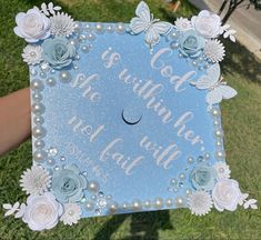 someone is holding up a blue graduation cap with flowers and pearls on it in the grass