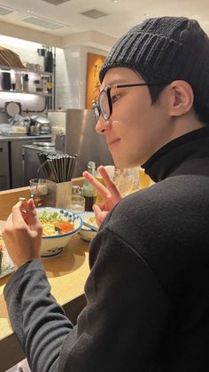 a man sitting at a table with food in front of him and making the peace sign