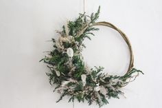 a wreath with white flowers and greenery hanging on the wall in front of a white wall