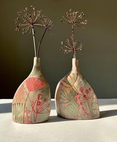 two vases with flowers in them sitting on a white tableclothed surface, one has pink and green designs