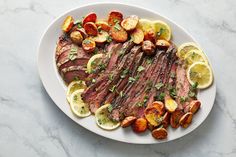 a white plate topped with steak, potatoes and lemons on top of a marble table