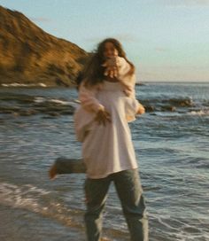 a woman walking on the beach with her dog in her arms and she's smiling at the camera