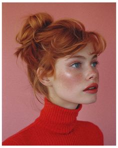 a woman with red hair and blue eyes wearing a red turtle neck sweater looking to the side