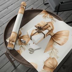 a table with wrapping paper and scissors on it, next to a roll of ribbon