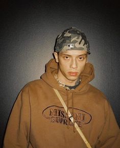 a young man wearing a brown hoodie and camo cap