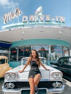 a woman sitting on the hood of a car in front of a drive - in