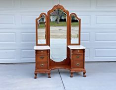 an antique vanity with mirror and stool in front of a garage door on a driveway