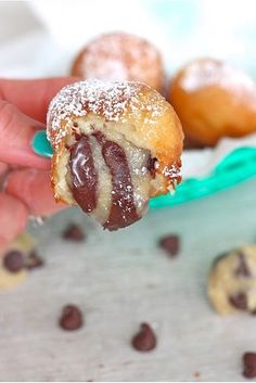 a hand holding a half eaten chocolate covered doughnut in front of other cookies and muffins